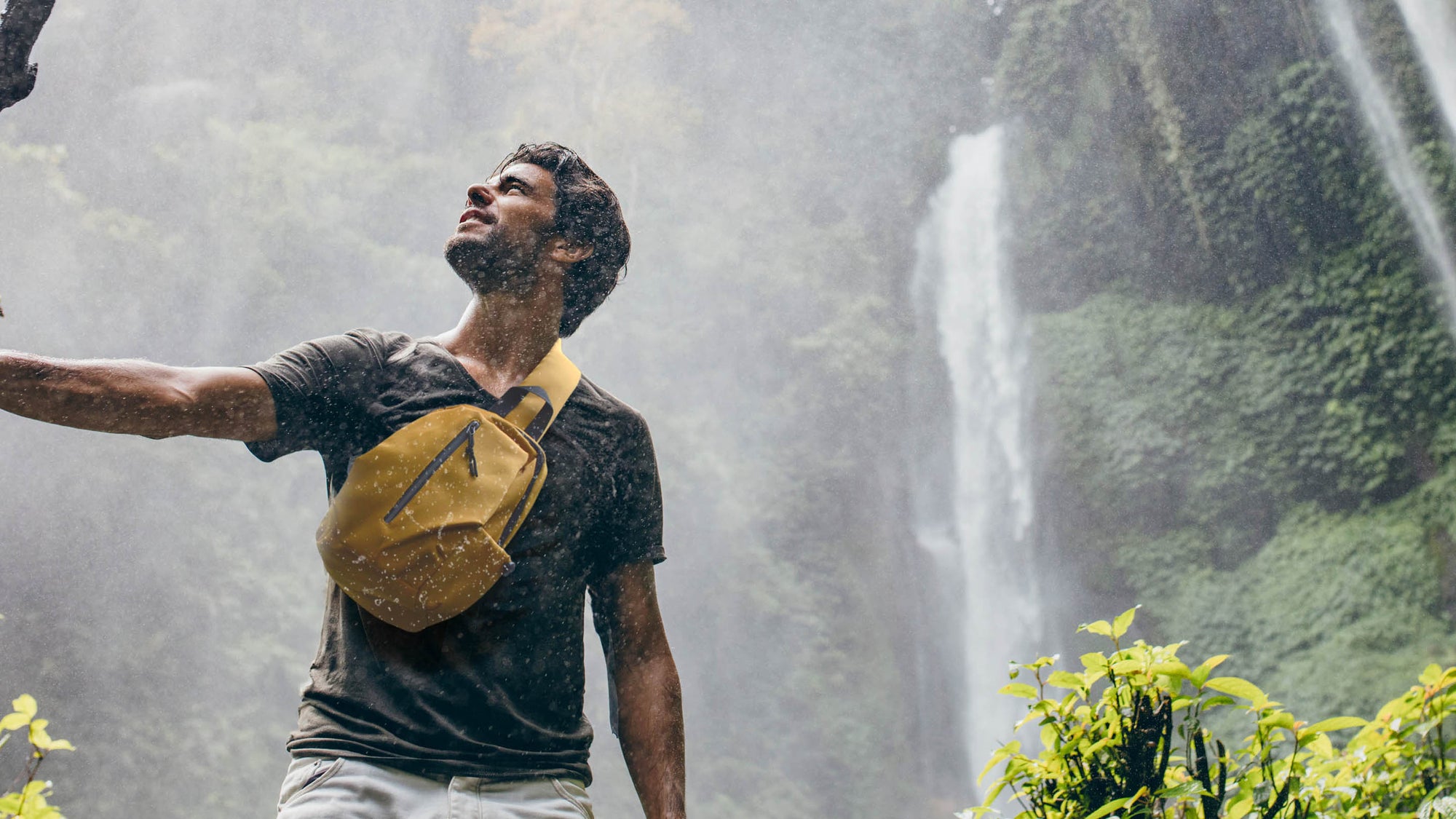 man wearing a yellow calla bag under a waterfall