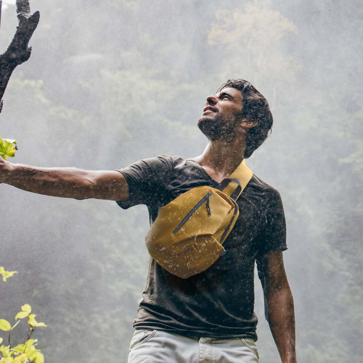 man wearing yellow cross body bag under a waterfall